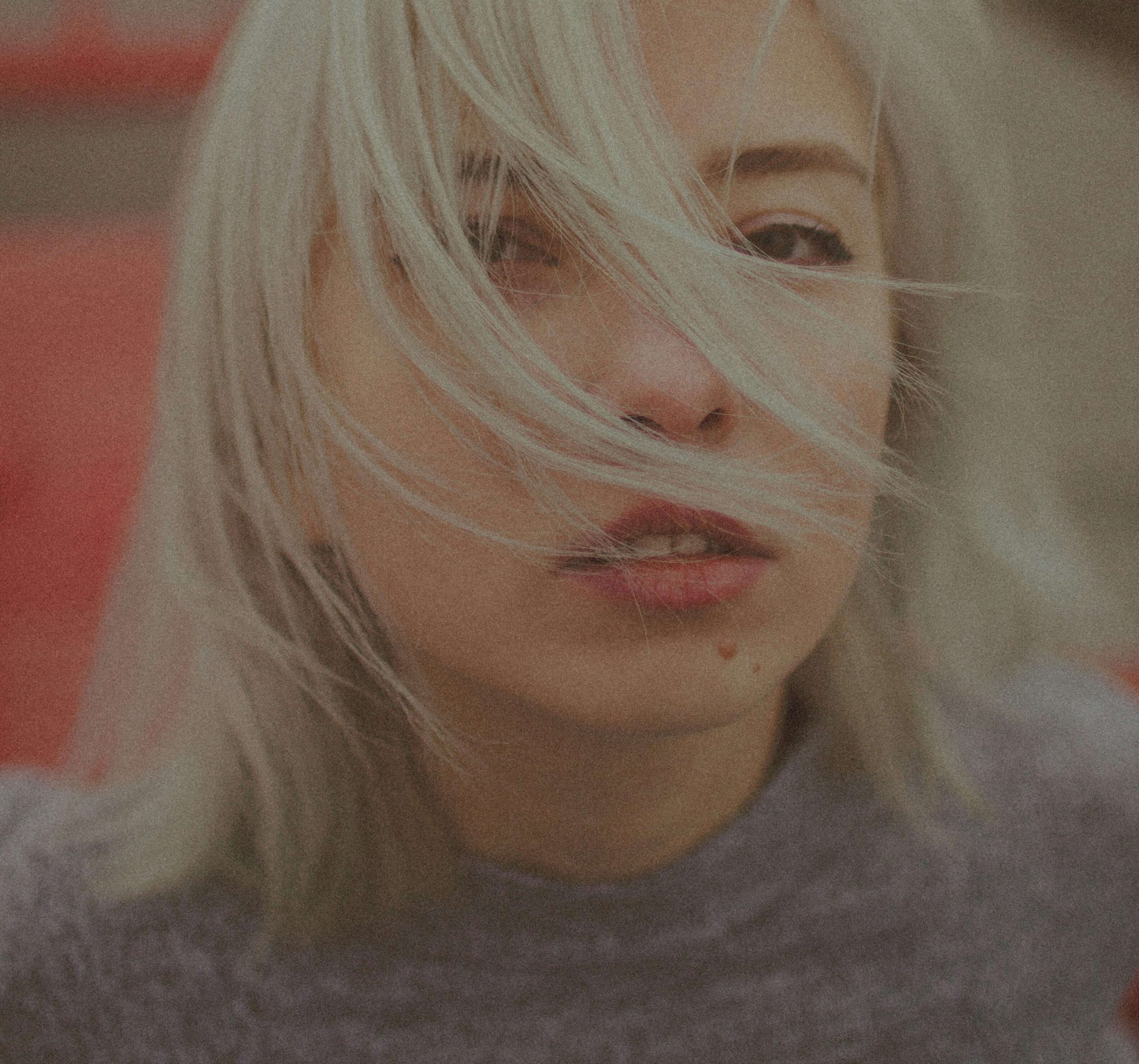 Photo d'une femme aux cheveux courts et blonds presque blancs, le visage partiellement caché par des mèches de ses cheveux au vent.
