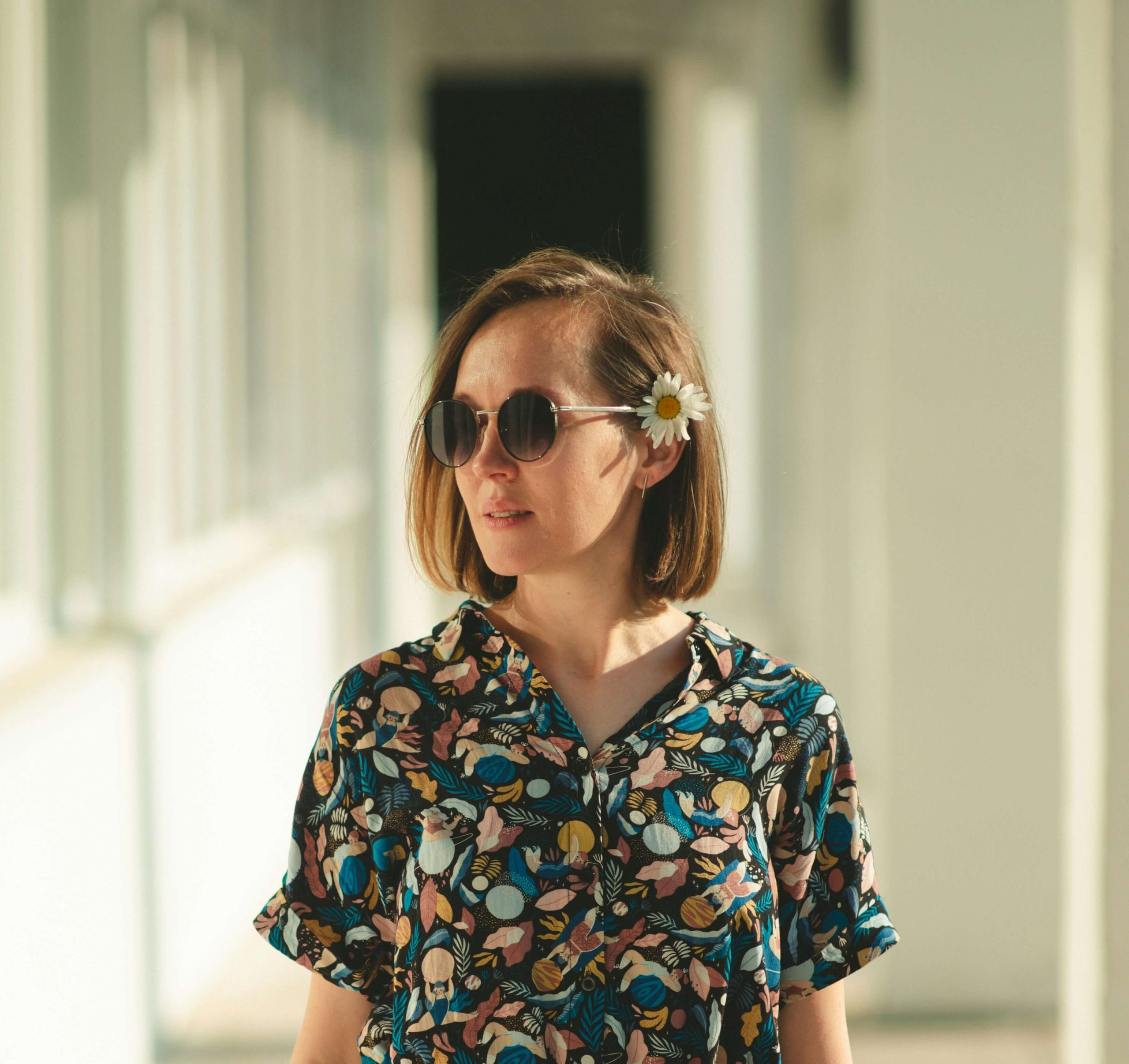 Personne portant des lunettes de soleil et une chemise colorée, avec une fleur dans les cheveux.